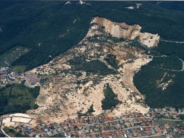 大規模な地すべりで住宅が下敷きになっている写真。
山側には明瞭な滑落崖が見られる。