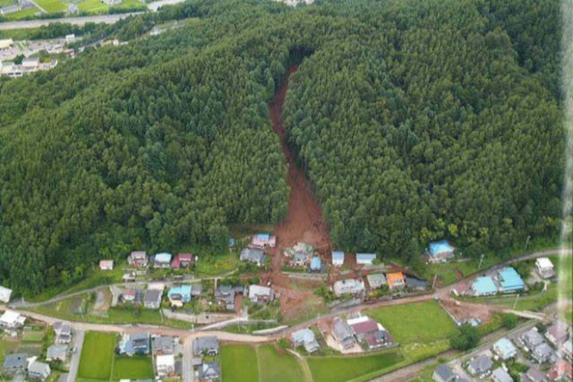 谷筋に沿って土石流が流下し、谷の出口で人家を巻き込んでいる写真。
