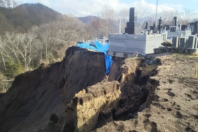 がけの上部が崩れ、崖上の墓地が崩落している写真。