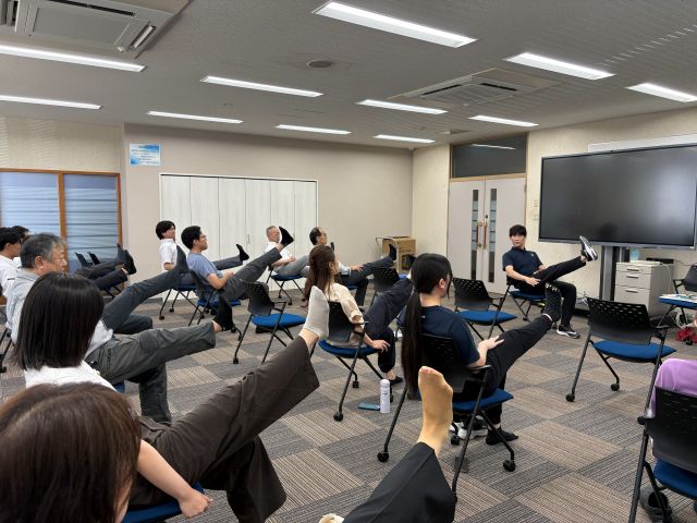 腿裏の筋肉を伸ばすストレッチを行う社員一同